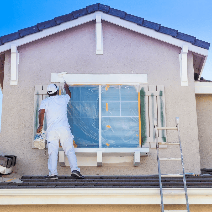 Man painting house window with white paint